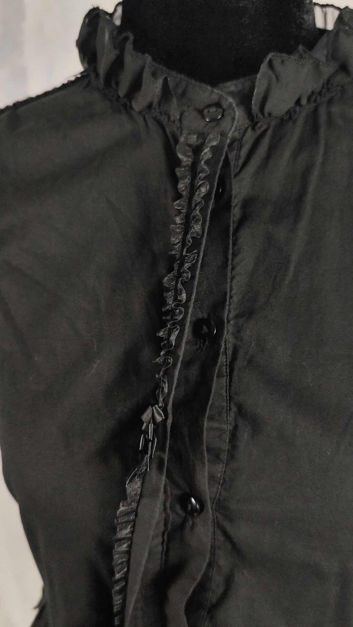 Close-up of a black ruffled dress with a high gathered neckline and decorative ruffle trim down the front, displayed on a dark mannequin torso.