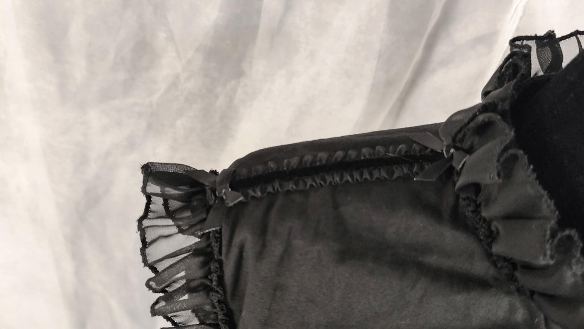 Close-up of a black ruffled and sheer mesh trim and a textured fabric background.