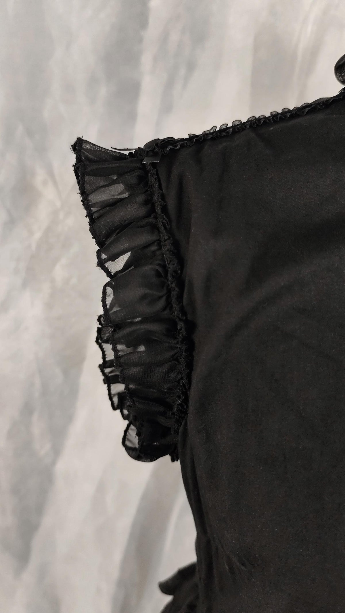 Close-up of a black dress featuring a sheer black ruffled trim along the edge, set against a textured gray background.