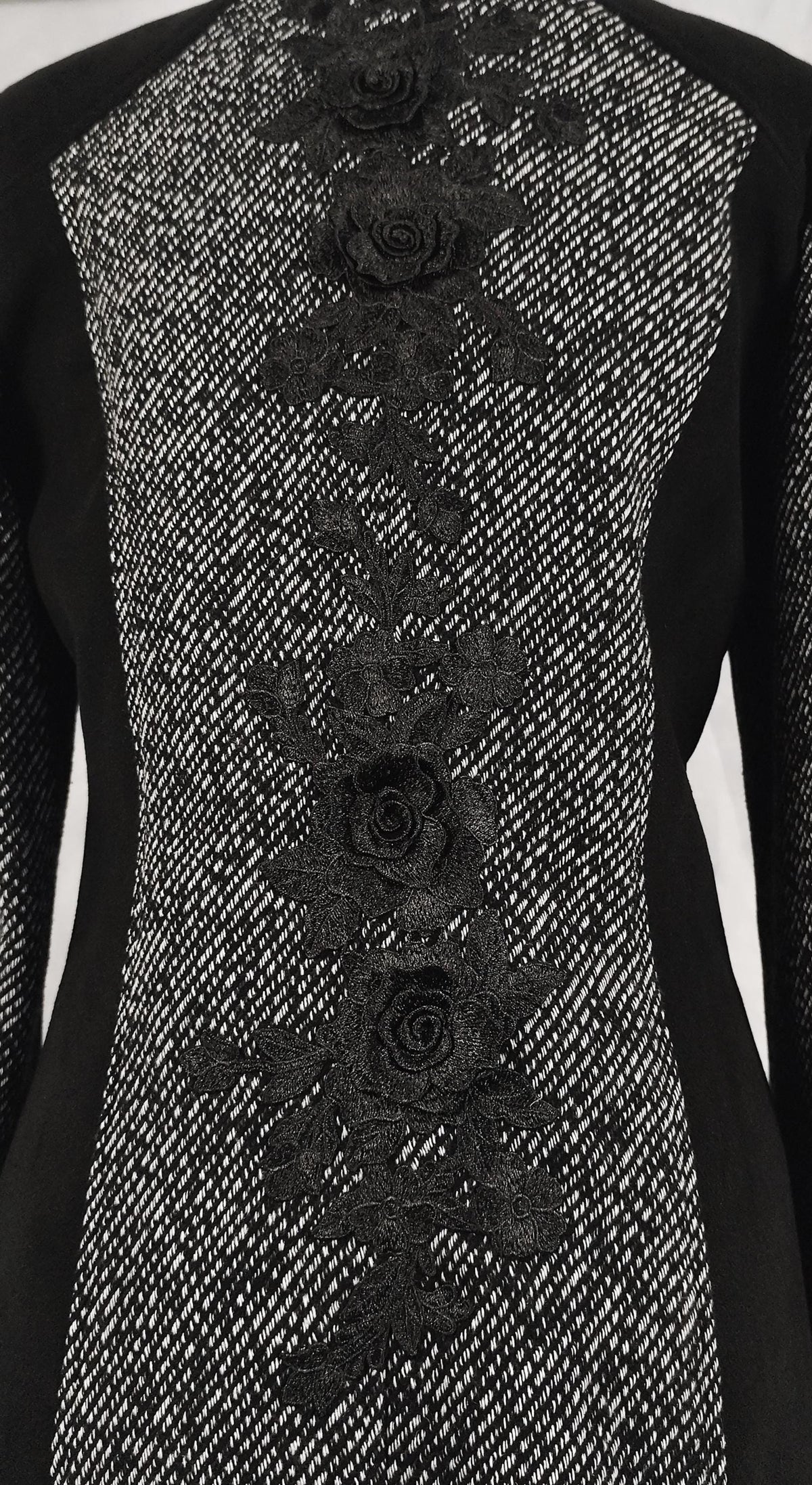 Close-up of a black and silver textured coat with vertical black floral lace applique down the center front.