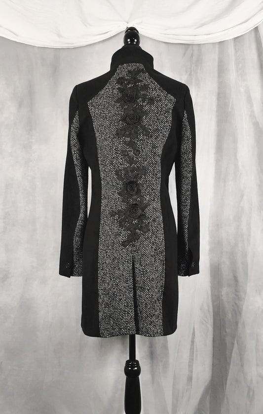 Back view of a black and gray patterned long coat displayed on a black dress form mannequin against a draped gray fabric backdrop.