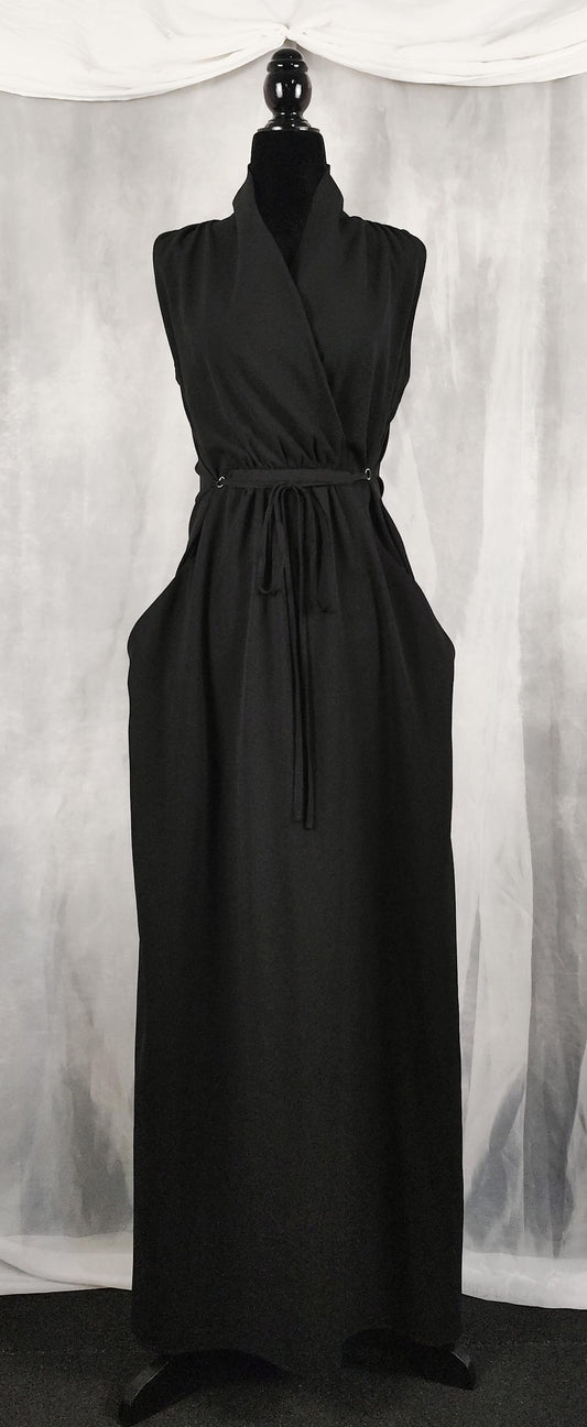 Front view of a sleeveless black maxi dress displayed on a mannequin. The dress features a crossover V-neckline, an adjustable drawstring waist tie, and a long, flowing skirt with side pockets