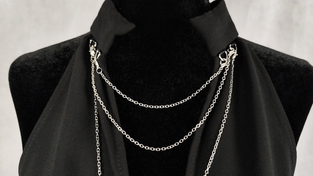 Photo detail of removable silver chains on the collar of a black tunic.