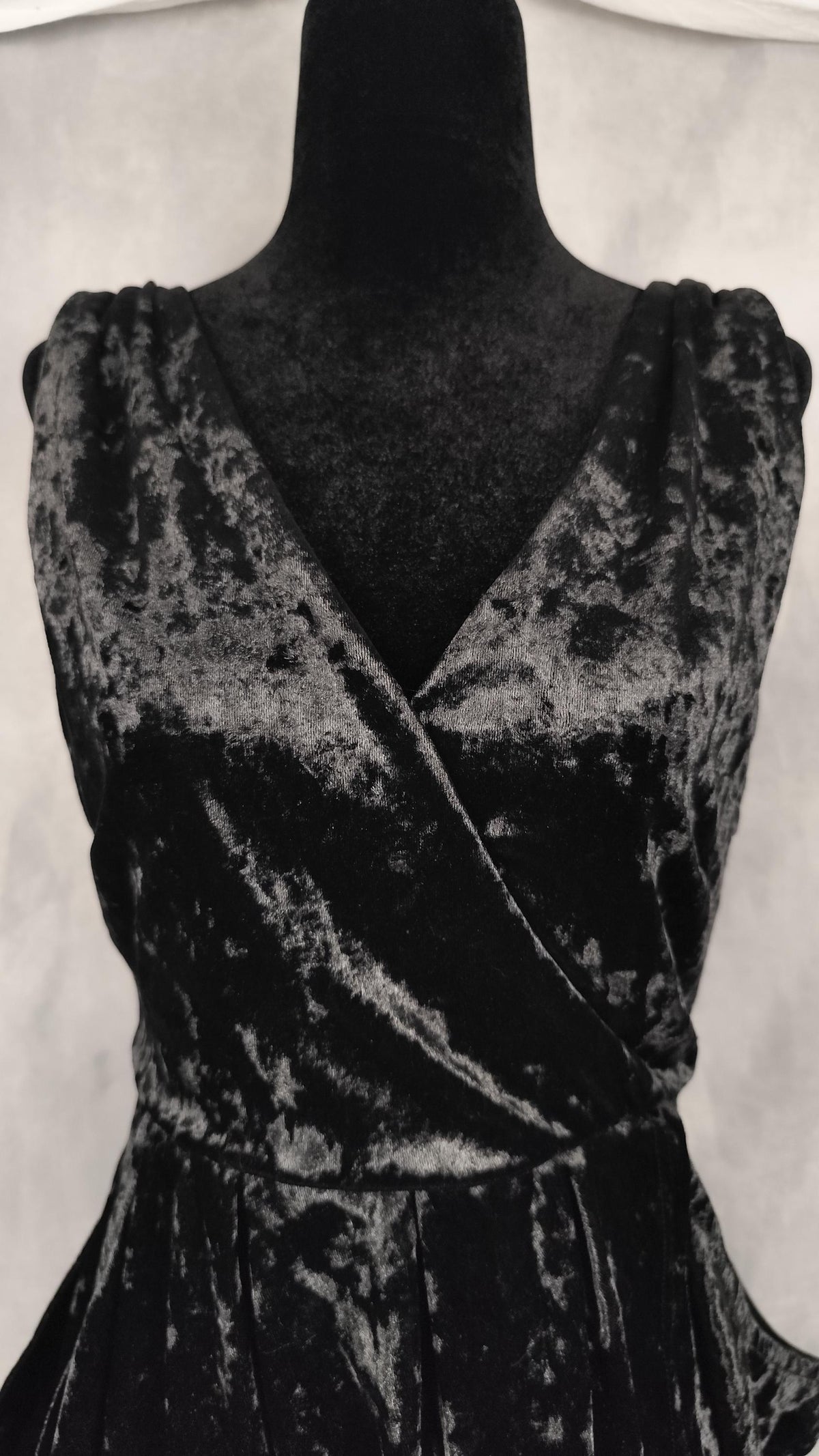Black crushed velvet wrap dress displayed on a black mannequin torso against a light gray fabric backdrop.