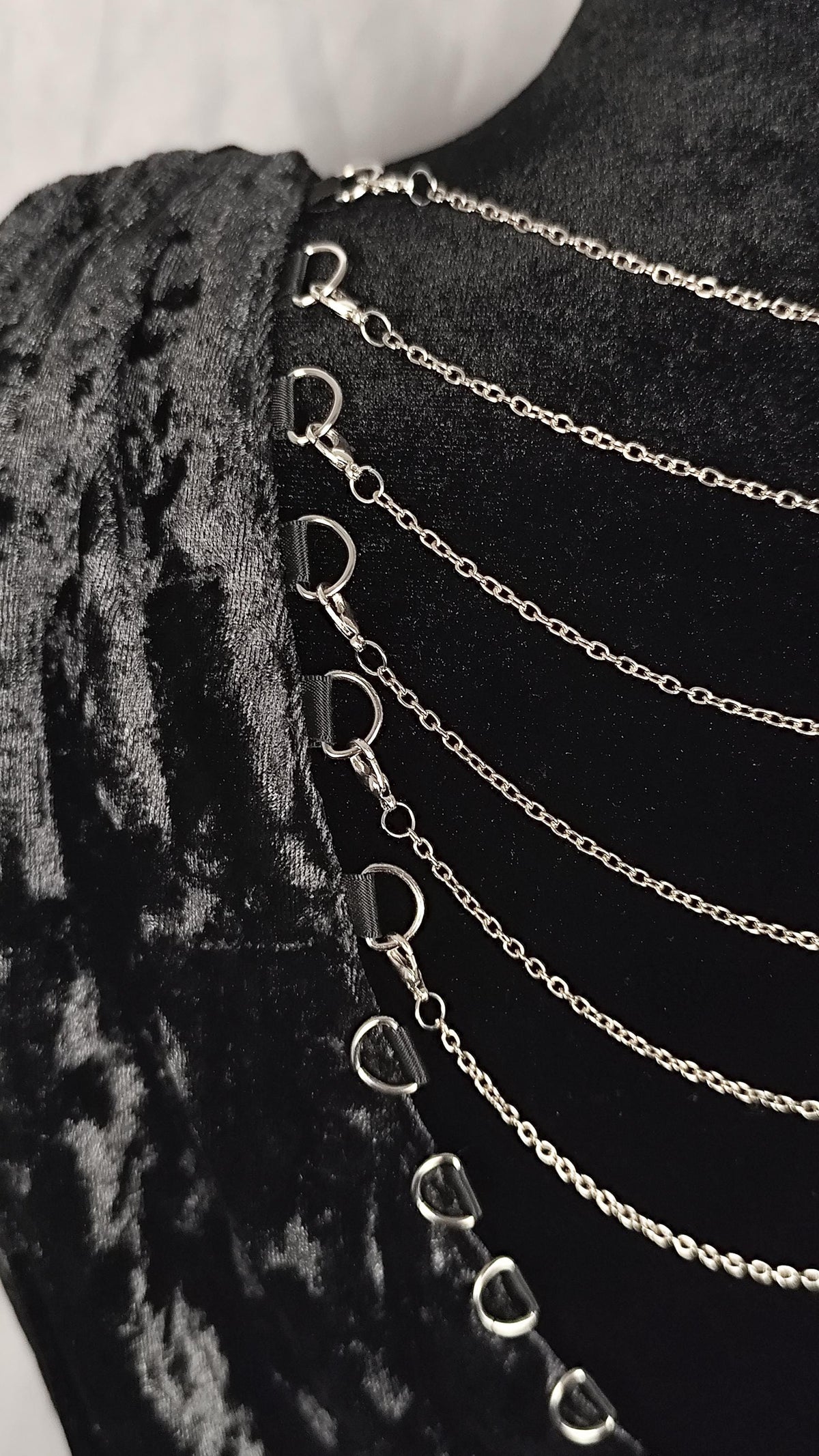 A close-up of a black velvet garment with multiple draped silver chains and metal ring connectors along the side.