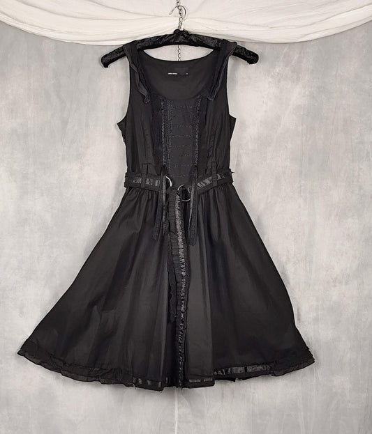 Front view of a black sleeveless dress with a structured corset-style bodice, and matching belt, hanging on a black hanger against a textured gray backdrop.