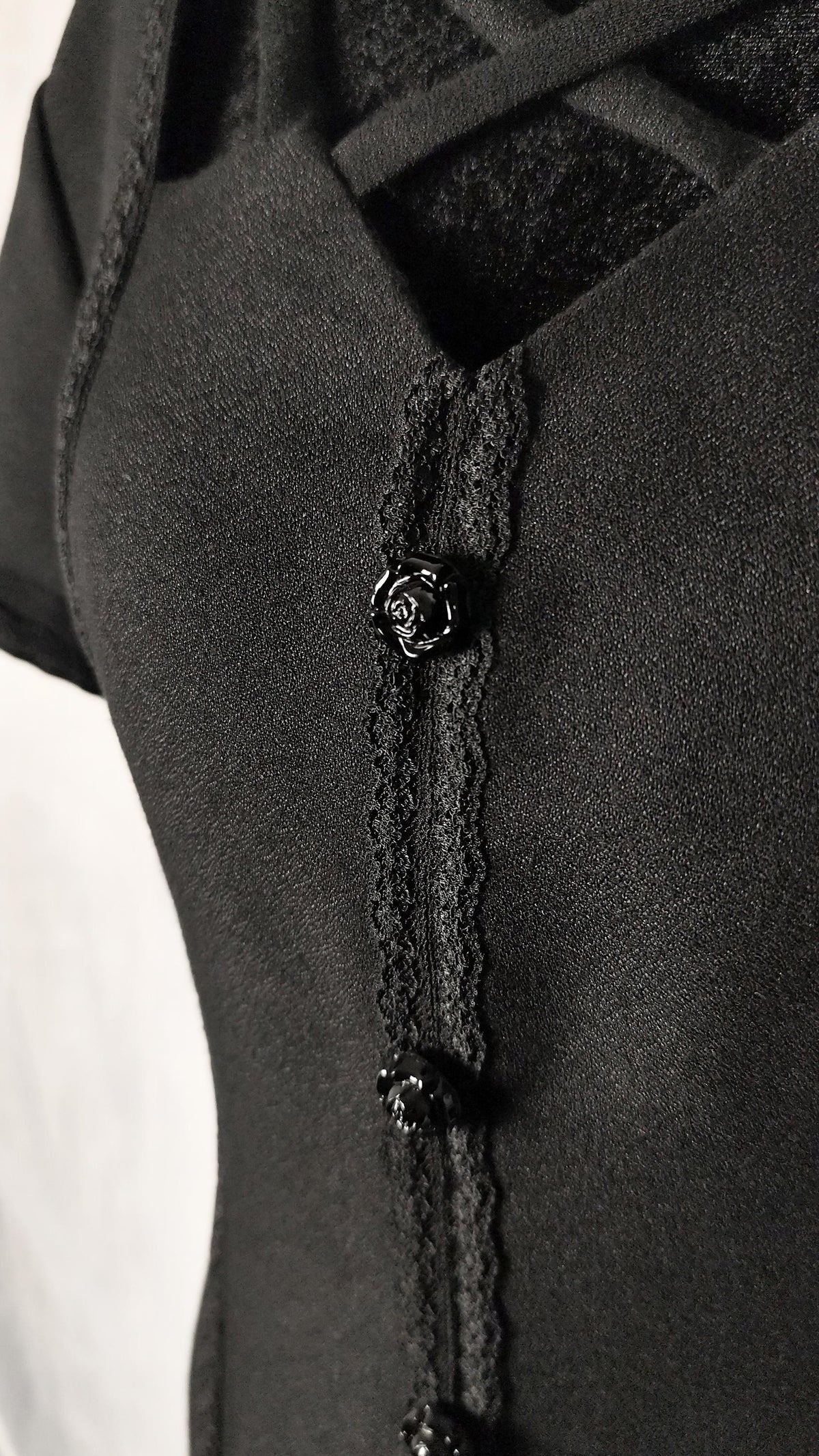 Close-up of a black short-sleeve midi dress with a lace-trimmed front placket, decorative flower black buttons.