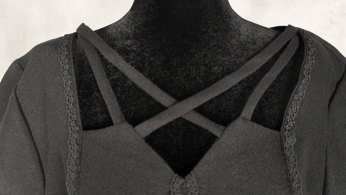 Close-up of a black midi dress neckline displayed on a black mannequin torso, featuring lace trim along the edges.