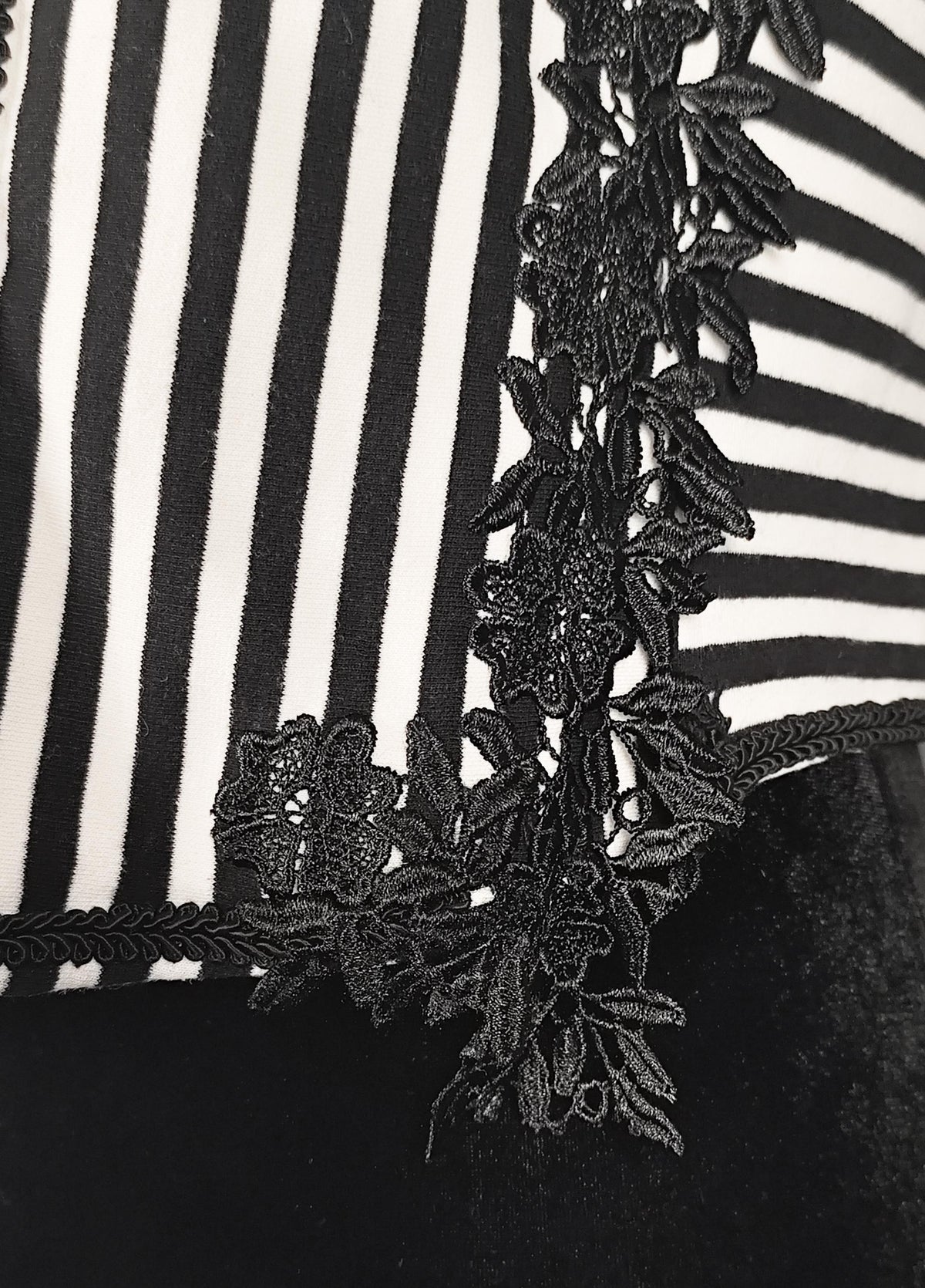 Close-up of a black and white striped shrug with a prominent black floral lace applique trim.