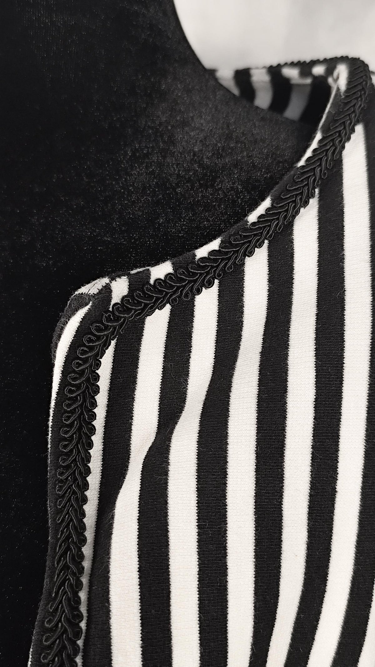 Close-up of a black and white vertically striped shrug with a black braided trim along the neckline, displayed on a black mannequin torso.