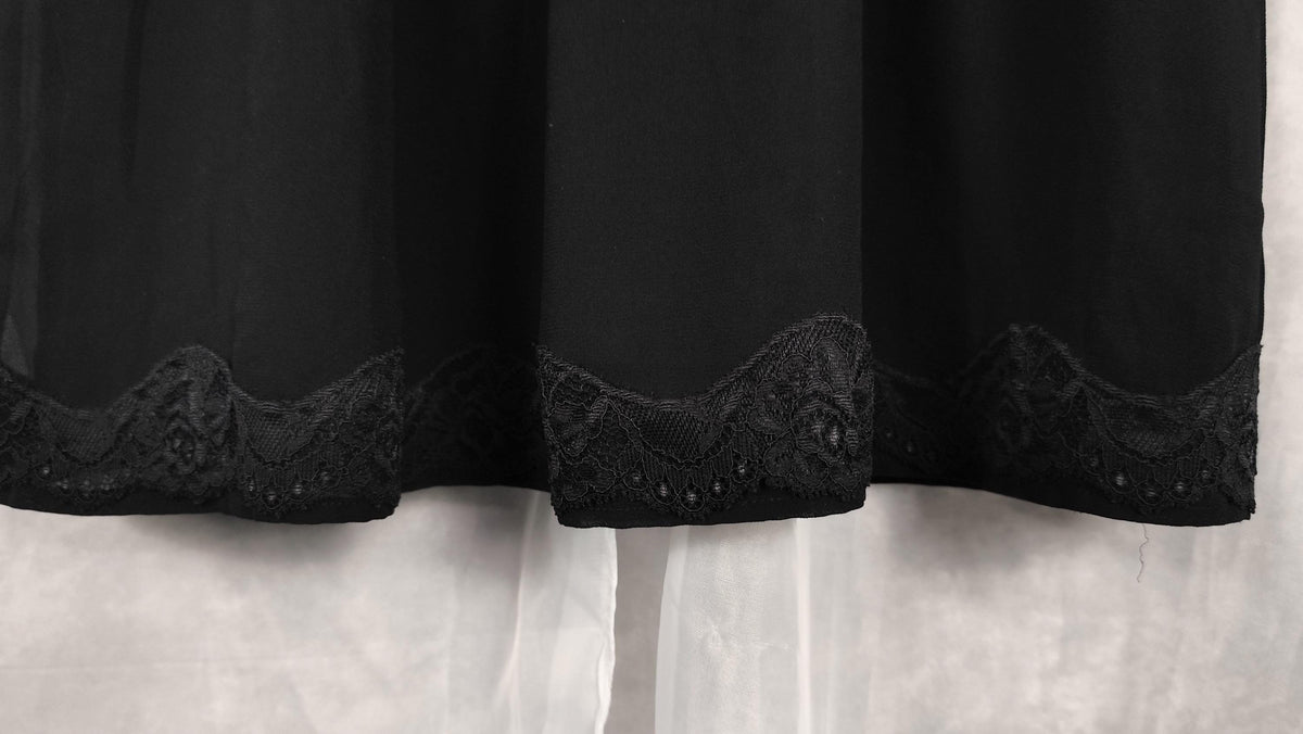 Black midi dress with a decorative black lace hem, shown hanging against a white background.