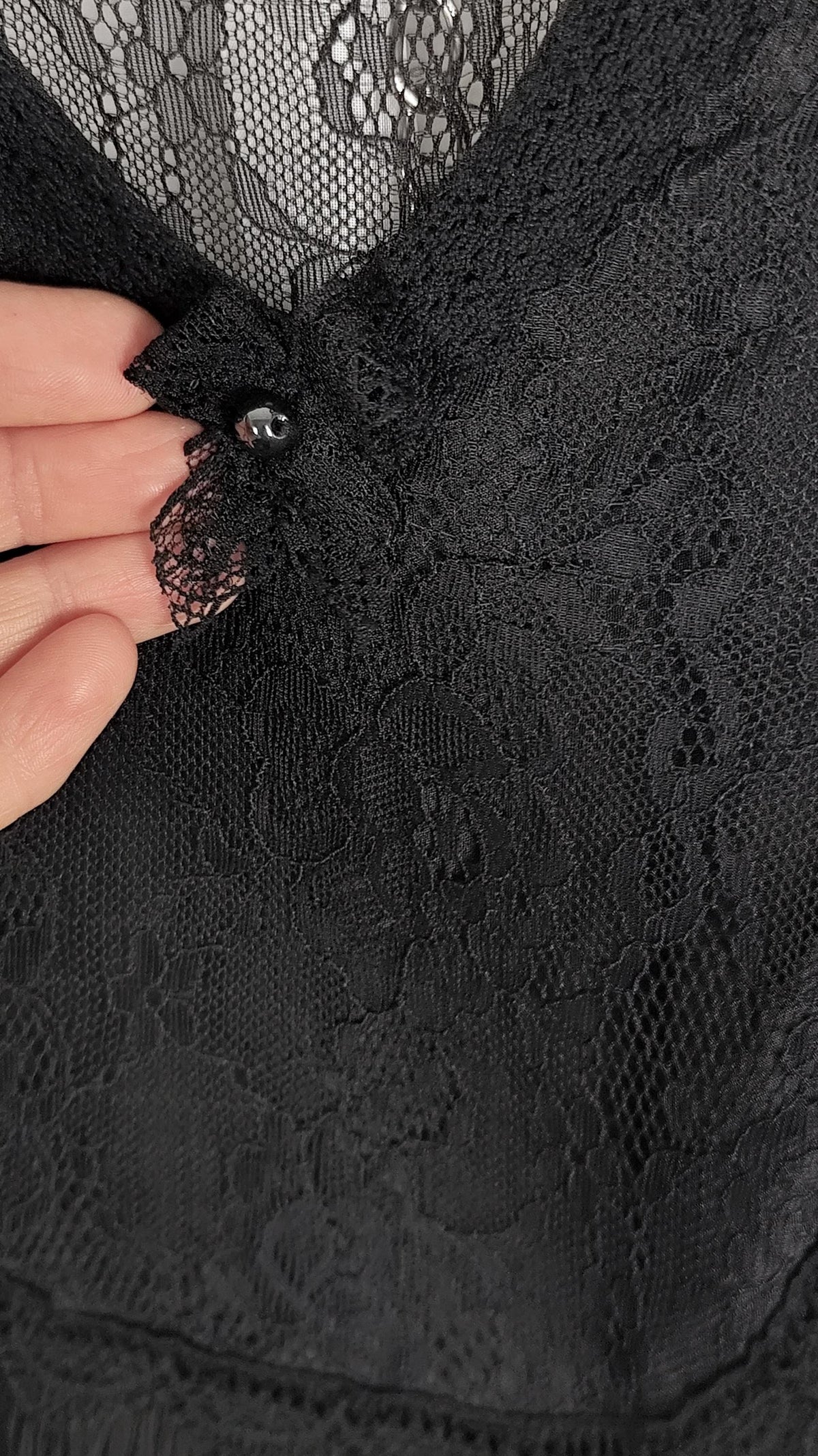 Close-up of a black lace garment with a hand holding a small decorative embellishment near the neckline.