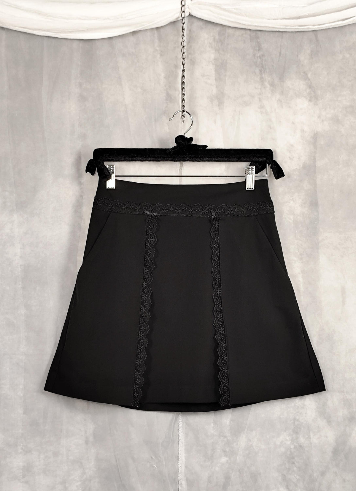 A black A-line short skirt with decorative lace trim down the front.