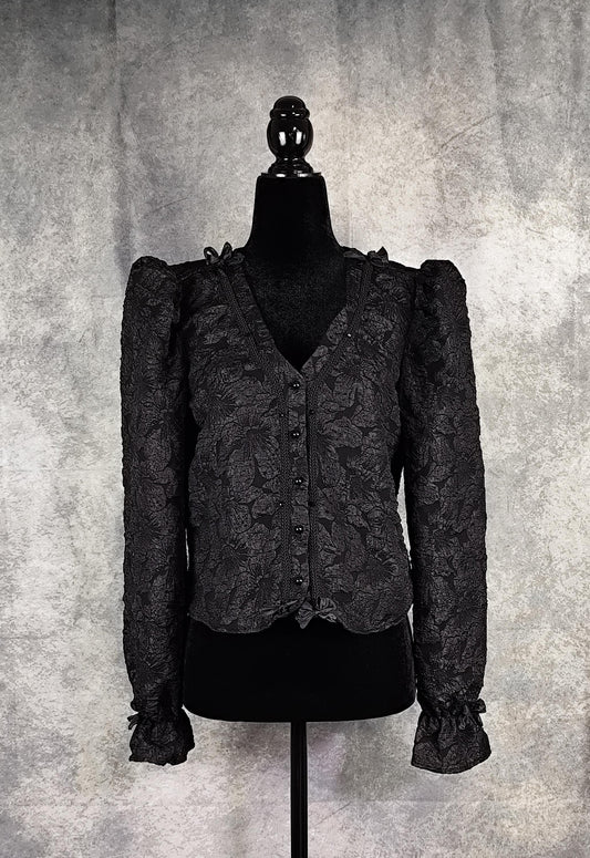 Front view of a black floral brocade blouse with black pearl-shaped buttons and braid trim.
