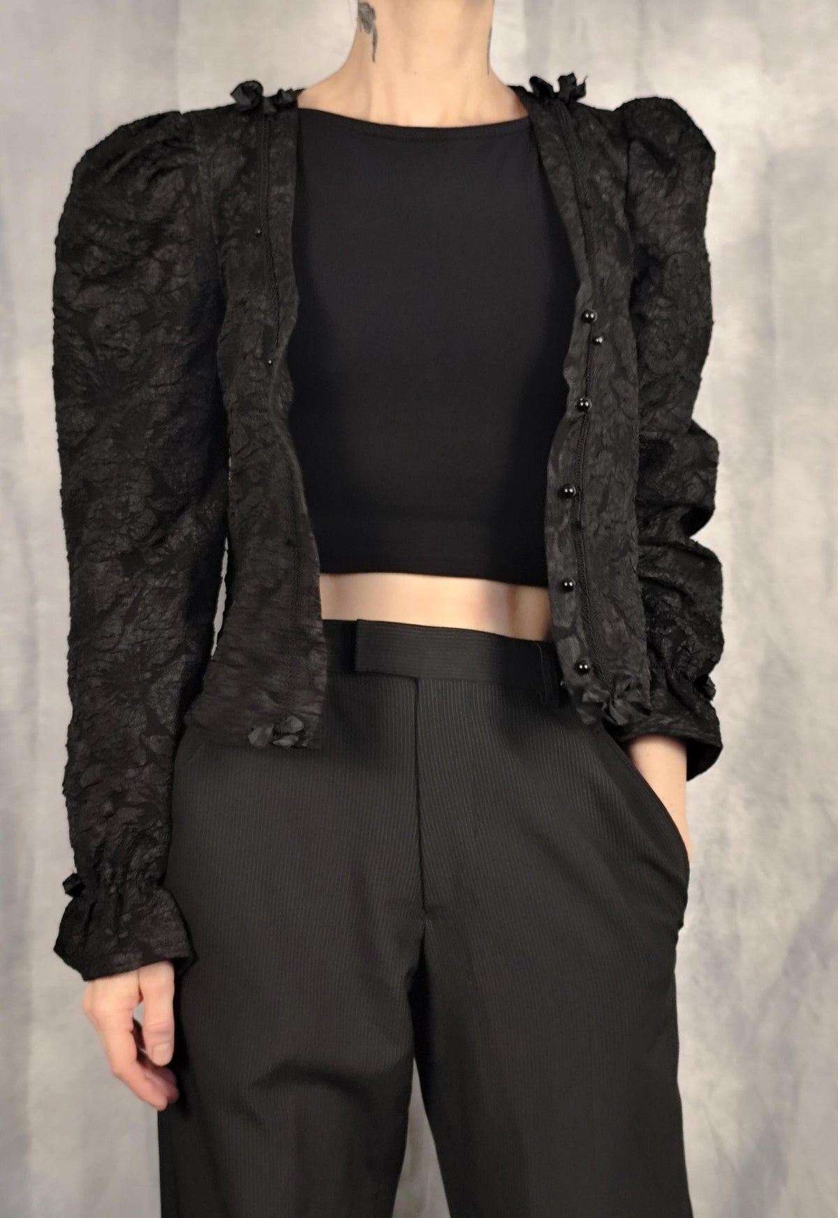Model wearing a black gothic brocade blouse, with black pearl-shaped buttons, braid trim, bows and puff longsleeves.