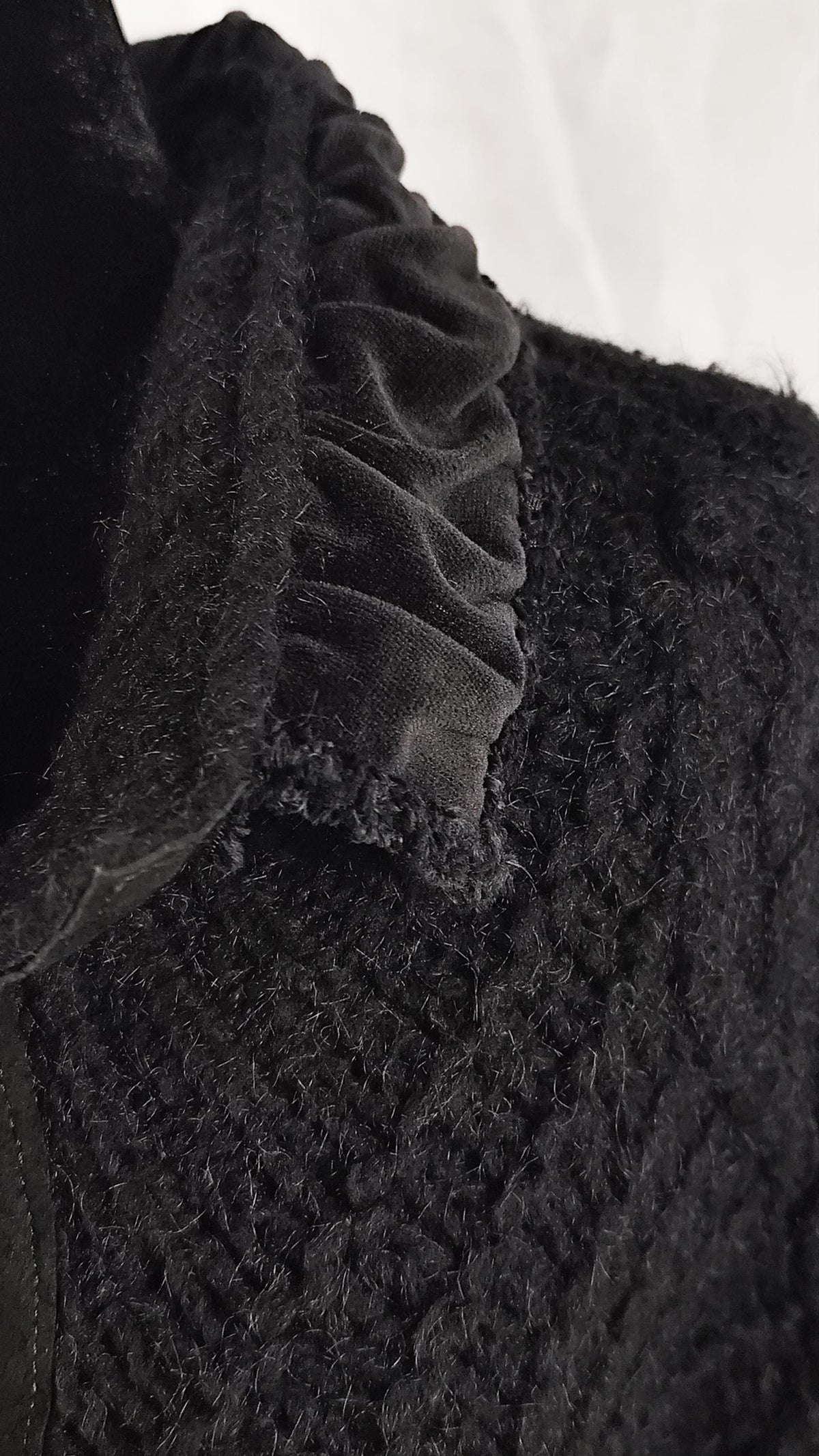 Close-up detail of a black textured knit jacket with a gathered black velvet ruffle trim along the neckline.