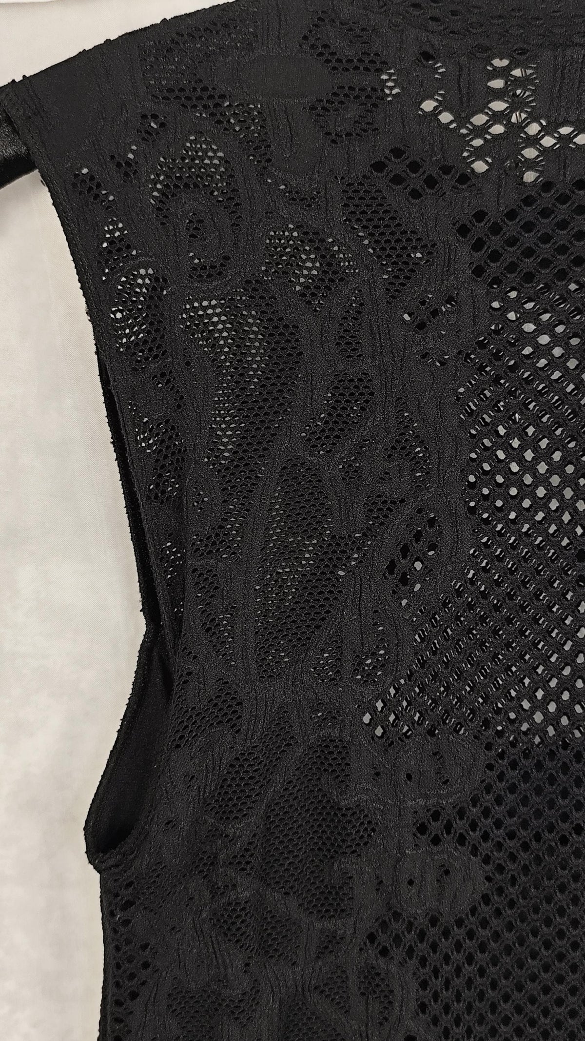 Close-up of a black sleeveless lace and mesh dress, showing intricate floral lace patterns and openwork mesh details against a light neutral background.