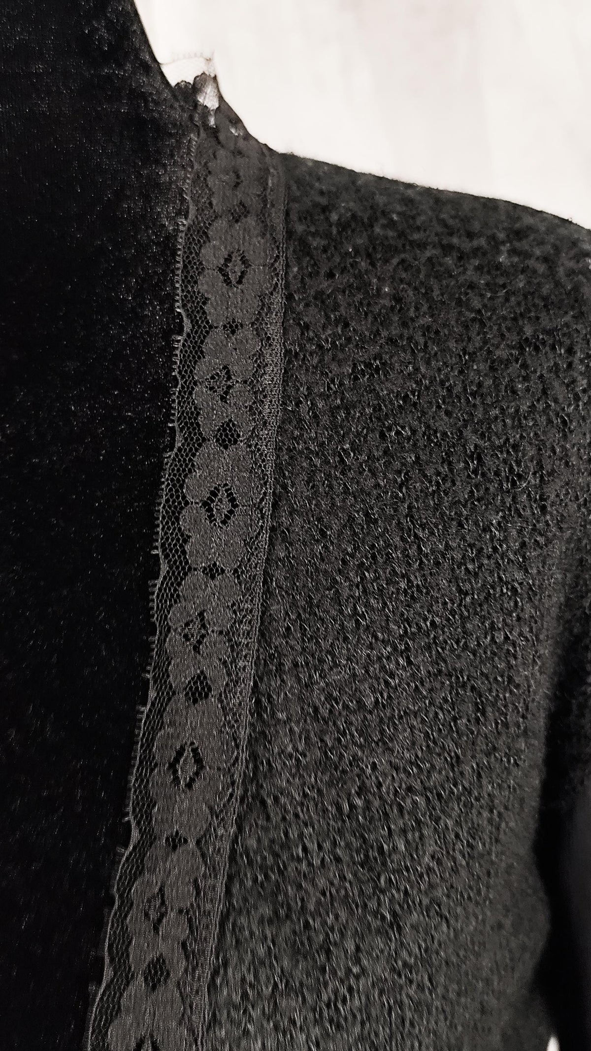 Close-up of a black textured knit garment with a wide black lace trim panel along the neckline.