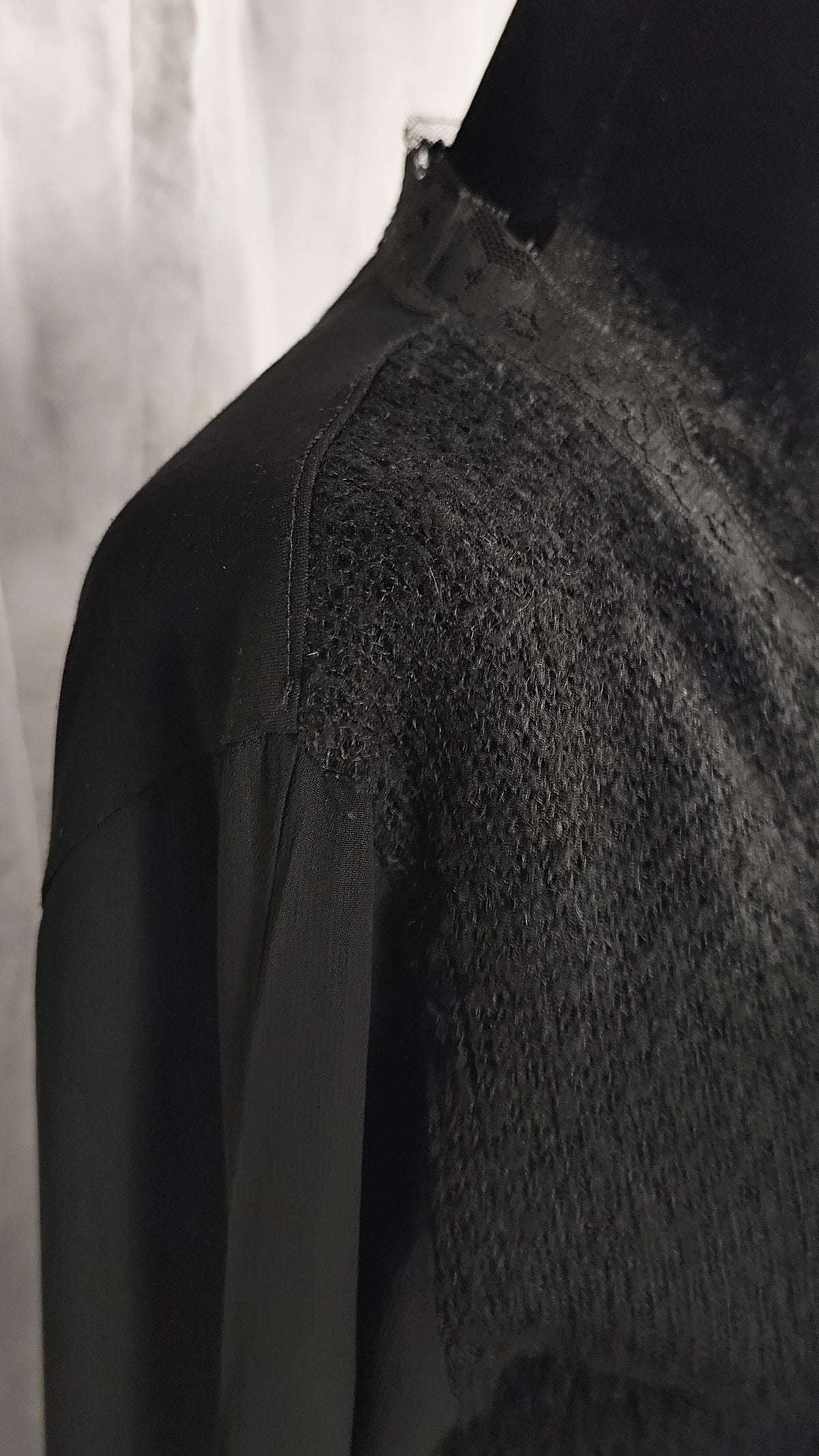 Close-up of a black long-sleeve cardigan with a knit yoke panel on the upper chest and shoulder.
