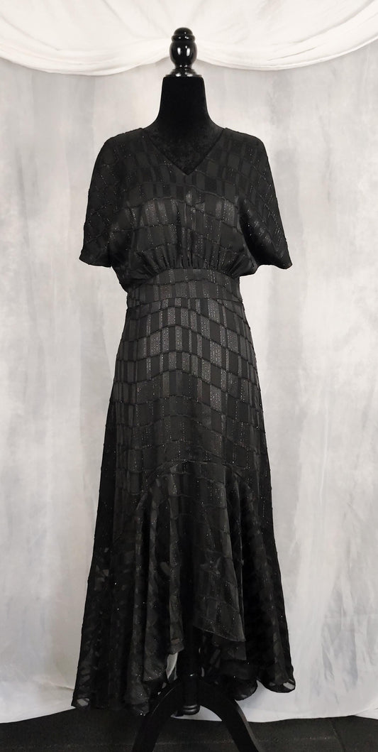 Front view of black mullet dress with short sleeves and a textured geometric pattern, displayed on a black mannequin against a draped white fabric backdrop.