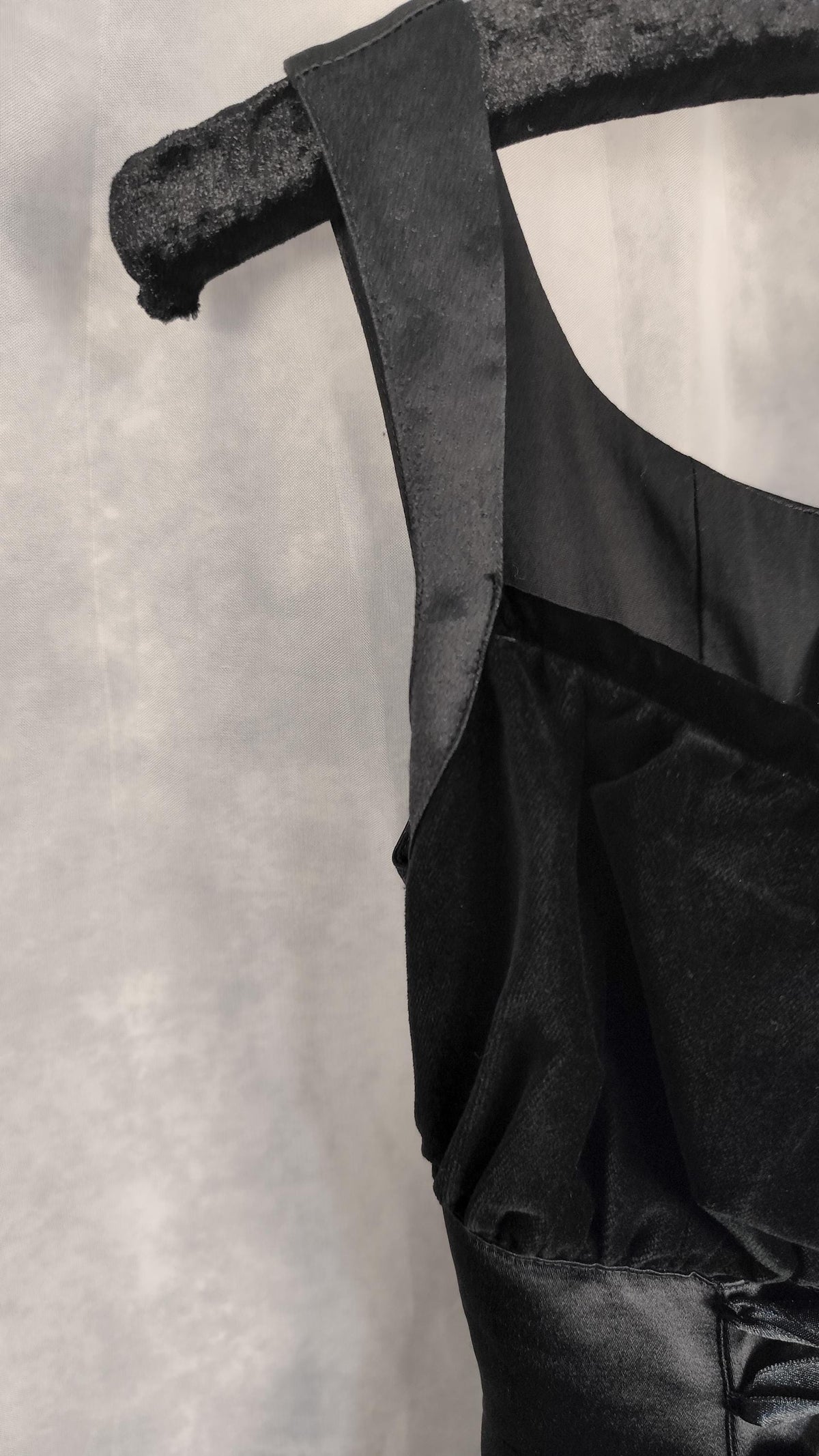 Close-up of a black satin dress hanging on a textured black hanger against a light gray backdrop.
