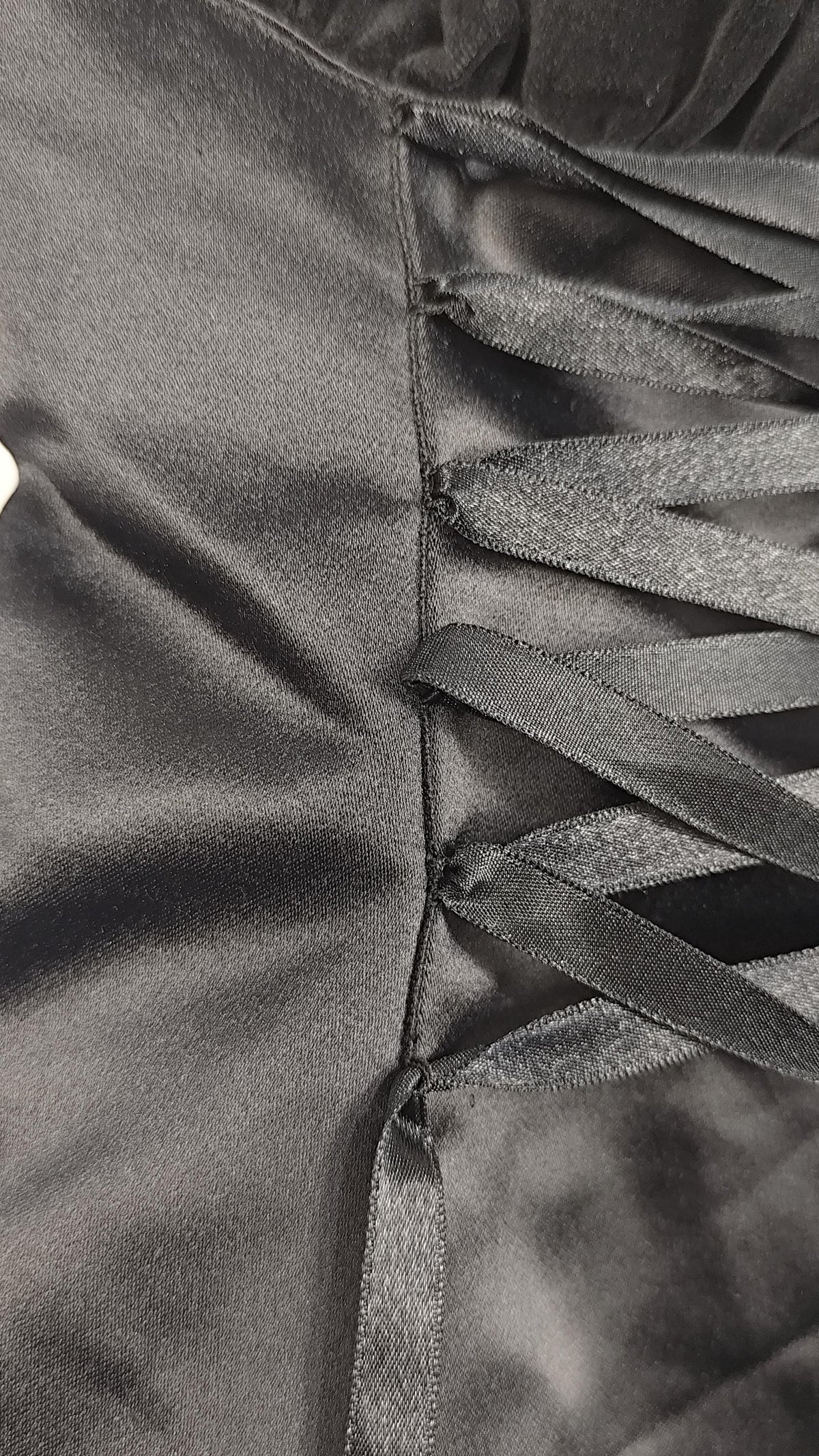 Close-up of a black satin dress with a vertical seam and multiple diagonal lace-up ties running down the center.