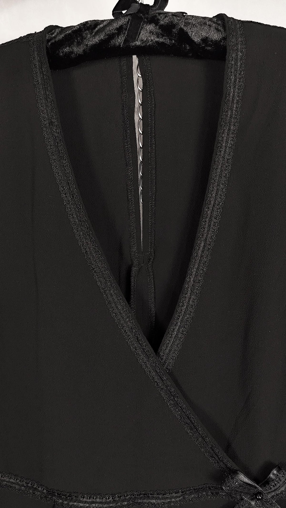 Close-up of a black wrap-style dress with a deep V-neck, black trim shown on a hanger against a dark background.